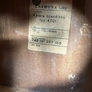 Detail štítku uvnitř akustické kytary z dřevěného povrchu. Na žlutém štítku je uveden nápis STÁTNÍ PODNIK, logo s číslem 33 a text CREMONA Luby. Dále…