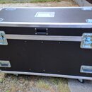 Černý transportní flightcase s hliníkovými hranami a rohy. Na přední straně jsou dvě stříbrné zapínací zámky a v horní části jedna černá rukojeť. V d…