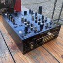 Černý DJ mixér značky Pioneer DJ, model DJM-450. Na horní části jsou umístěny posuvníky a zahlreiche ovládací knoflíky, na zadní straně jsou různé ko…