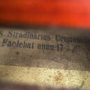 Detailní záběr na vnitřní štítek smyčcového nástroje. Na štítku je černým tiskem text „Stradivarius Cremonensis Faciebat anno 17“. Papír štítku je ze…