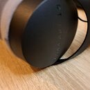 Detailní pohled na pravou mušli černých sluchátek s šedým polstrováním. Na vnější straně mušle je vyrazen nápis DT 770 PRO X. Povrch plastu je matní…