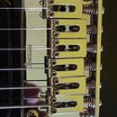 Detailní záběr na chromovaný kobylku elektrické kytary s mechanismem tremolo. Na kovové základní desce je vlevo vyražen nápis Ibanez. Povrch je leskl…