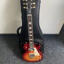 Elektrická kytara s červeně-žlutým sunburst povrchem a černým hmatníkem s trapezoidními vložkami. Na hlavě je zlatý nápis Gibson a pod ním kurzivní n…