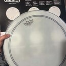 Bílá bubenová koženka s logem REMO a nápisem POWERSTROKE PE COATED MADE IN U.S.A. Koženka má v dolní části dvě soustředná šedá kruhová vymezení. V po…