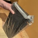 Černý klávesový nástroj zabalený v průhledném plastovém obalu. Horní část přístroje je stříbrná. Na zařízení nejsou vidět žádné značky ani nápisy.
