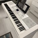 Bílá digitální pianola s klávesnicí a integrovanými reproduktory. Na ovládacím panelu je vidět logo YAMAHA a nápis Clavinova. Na notovém stojanu je u…