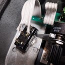 Detailní pohled do vnitřku přístroje na elektronické součástky a zapojení. Je vidět černý plastový konektor s připojeným bílým plochým kabelem a část…