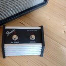 Černý nožní spínač s bílým žebrovaným spodním tělem a dvěma červenými tlačítky. Na horním černém panelu je bílé logo Fender a nápisy CH SELECT a EFFE…
