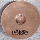 Kruhový mosazný činel s viditelným kovánívým povrchem a vyvýšeným středem. Ve spodní části je černý nápis pAisTe a pod ním menší text MADE IN SWITZER…