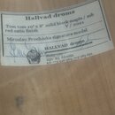Detailní záběr na bílý papírový štítek nalepený na světlém dřevěném povrchu. Na štítku je text: „Hallvad drums“, „Tom tom 10" x 8" solid block maple…