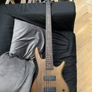 Hnědá elektrická basová kytara s přírodním dřevěným povrchem a tmavým hmatníkem. Na hlavě je viditelný nápis "Squier". Nástroj má dva široké černé sn…
