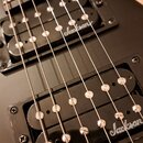 Detailní záběr na černou elektrickou kytaru s dvěma humbuckery. Na obou snímačích je bílý nápis Jackson. Povrch nástroje má matný černý finish, hardw…