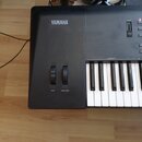 Černý digitální klavír s bílými a černými klávesami. Na horní části je bílý nápis YAMAHA a pod posuvníky jsou nápisy PITCH a MODULATION. Povrch nástr…