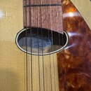 Detailní pohled na hmatník a ozvukovou otvory akustické kytary s dřevěnou deskou světlé barvy a hnědým pickguardem s mramorovaným vzorem. Uvnitř otvo…