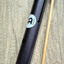Černý kovový Percussion Tube s doprovodným beaterem ze světlého dřeva s černou gumovou hlavicí. Na trubici je bílý oválný štít s černým logem a nápis…