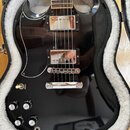 Černá elektrická kytara s lesklým povrchem v otevřeném kufru s bílou vnitřní výstělkou. Nástroj má dva chromované humbuckery, chromovaný kobylník a s…