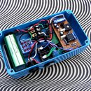 Fotografie zachycuje otevřený modrý kovový box s vnitřním zapojením efektového pedálu. Uvnitř je vidět elektronický obvod na perforované desce, dvě p…