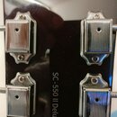 Detail hlavy elektrické kytary v černé barvě s chromovanými ladicími kolíky. Na povrchu je bílý nápis SC-550 II Deluxe a štítek s texty RoHS CE UK CA…