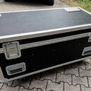 Černý transportní flightcase s hliníkovými hranami a rohy. Na horní části je nalepená malá bílá nálepka s modrým logem. Boční stěna obsahuje dvě madl…