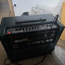 Tmavě zelený kytarový kombozesilovač s texturovaným povrchem a černou rukojetí. Na předním panelu jsou ovládací knoflíky a nápisy „Hughes & Kettner“,…