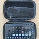 Černý přenosný sekvencer Roland P-6 v černém zipovém pouzdře s vnitřní síťovou kapsou a přiloženým kabelem. Zařízení má digitální displej, řadu bílýc…