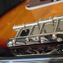 Detailní záběr na chromovaný kobylkový mechanismus elektrické kytary s tělem v barevnosti sunburst. Jsou vidět čtyři stáčecí šrouby pro ladění intona…