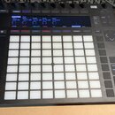 Černý MIDI kontrolér s mřížkou 8x8 bíle podsvícených padů. V horní části je digitální displej zobrazující hodnoty jako 250 Hz, -13.7 dB, -3.21 dB, 4.…
