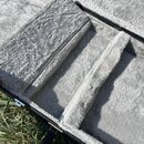 Detail vnitřku kufru s šedým, huňatým polstrováním. V prostoru jsou vidět dvě vyvýšené přepážky stejného materiálu. Kufr má černý vnější rám s kovový…