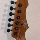 Fotografie zachycuje hlavu elektrické kytary z hnědého dřeva s šesti černými ladičkami. Na povrchu je bílý nápis "Zet" a menší svislý text "GUITARS".…