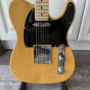 Elektrická kytara typu Telecaster s přírodním dřevěným povrchem těla a javorovým hmatníkem. Má černý pickguard a chromované kovové části, včetně kryt…