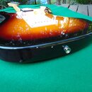 Elektrická kytara s lakovaným povrchem v přechodové barvě od žluté přes oranžovou po černou. Nástroj má bílý pickguard a černý humbucker v pozici u k…