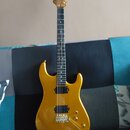Zlatá elektrická kytara s tvarem superstrat a hnědým hmatníkem. Nástroj má jeden humbucker v pozici mostu, dva snímače typu single-coil a zlatý hardw…