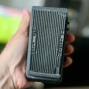 Černý kytarový pedál s texturovaným povrchem a svislým žebrováním. Na levé straně je vyražen nápis AMP TIER a na pravé straně IN INSTRUMENT. Povrch v…