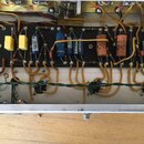 Fotografie zachycuje vnitřní zapojení elektronického zařízení s řadou komponentů na černé desce. Jsou zde vidět růnobarevné kondenzátory a rezistory…