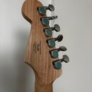 Zadní strana hlavy elektrické kytary z přírodního dřeva s šesti stříbrnými ladičkami. Na dřevě je černý nápis: Designed and Backed by Fender s/n CENG…