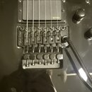 Detailní pohled na černý snímač a kobylku elektrické kytary. Na snímači je bílý nápis EMG a na kobylce nápis Floyd Rose. Povrch je černý, s viditelný…