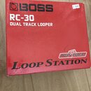 Červená kartonová krabice s nápisy. V horní části je černé logo BOSS a bílý text RC-30 DUAL TRACK LOOPER. V dolní části je logo TWIN PEDAL a velký če…