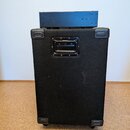 Černý reproduktorový box potažený texturovaným materiálem s plastovými rohy a madlem z černé plastu a kovu. Na horní části boxu je umístěn menší čern…