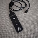 Černý přenosný audio rozhraní s připojeným kabelem USB-C. Na zařízení jsou bílé nápisy „Groove“ a „APOGEE“ spolu s logem značky. Uprostřed se nacháze…