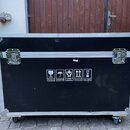 Černý transportní flightcase s hliníkovými hranami, rohovými zpevněními a dvěma zapínacími zámky. Na přední straně jsou bílé informační piktogramy s…