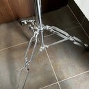 Fotografie zachycuje spodní část chromovaného stativu s rozkládacími nohami. Nohy jsou vyrobeny z kovových profilů a zakončeny gumovými patkami. Na p…