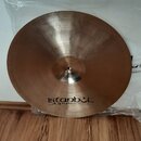 Kruhová kovová činely v bronzové barvě s jemným broušením povrchu. Ve spodní části je černý nápis istanbul Agop Made in Turkey. Činely stojí na dřevě…