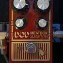 Červený efektový pedál s nápisy MEATBOX SUBSYNTH a logem dod. Na horní části jsou čtyři černé ovládací knoflíky s kovovými vršky a popisky SUB, LOW,…