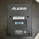 Zadní strana černého elektronického zařízení značky ALESIS. Uprostřed je bílá nálepka s textem „EU Address: InMusic GmbH | Harkortstr. 12-32 | 40840…