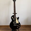 Černá elektrická kytara typu Les Paul značky Epiphone, umístěná na černém stojanu. Na hlavě hmatníku je bílý nápis Epiphone a vpravo pod ním kurzivní…