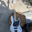 Bílá elektrická basová kytara s bílým hmatníkem z jasnu a černým pickguardem. Na hlavě je nápis Squier by Fender. Tělo nástroje vykazuje čistý povrch…