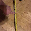 Fotografie zobrazuje kovový, stříbrný stojan nebo držák s černým plastovým knoflíkem na horním konci. Vedle předmětu je přiložen žlutý skladovací met…