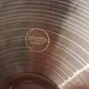 Detailní záběr na kovový povrch činely s koncentrickými drážkami. Uprostřed je vyryto logo Paiste a nápis HAND MADE IN SWITZERLAND v kruhovém uspořád…
