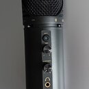 Černý kondenzátorový mikrofon s kovovou síťkou. Na těle jsou nápisy MUTE, GAIN a HEADPHONES u ovládacích prvků, dále označení modelu KM-2U a značka K…