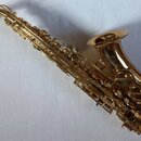 Zlatý lakovaný altový saxofon s mosazným povrchem. Na čáře nástroje je vyryto logo a nápis "YAMAHA". Povrch instrumentu je v čistém stavu bez viditel…